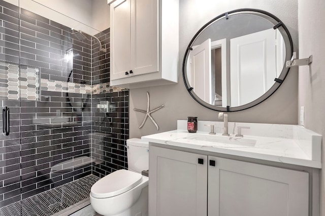 bathroom with toilet, a tile shower, and vanity