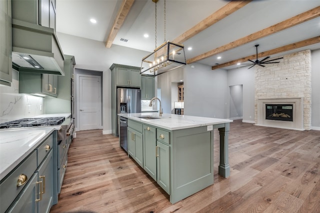 kitchen featuring beamed ceiling, a fireplace, light hardwood / wood-style floors, an island with sink, and pendant lighting