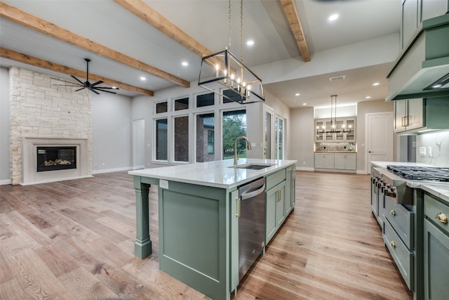 kitchen featuring beamed ceiling, light wood-type flooring, sink, a stone fireplace, and an island with sink