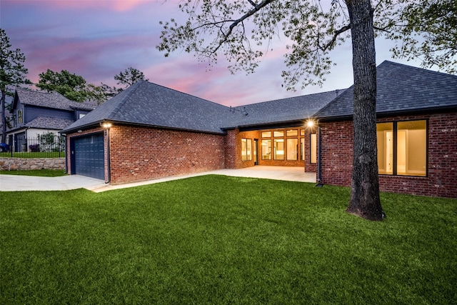 back house at dusk featuring a garage and a yard