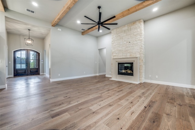 unfurnished living room featuring wood-type flooring, beam ceiling, ceiling fan with notable chandelier, and a fireplace