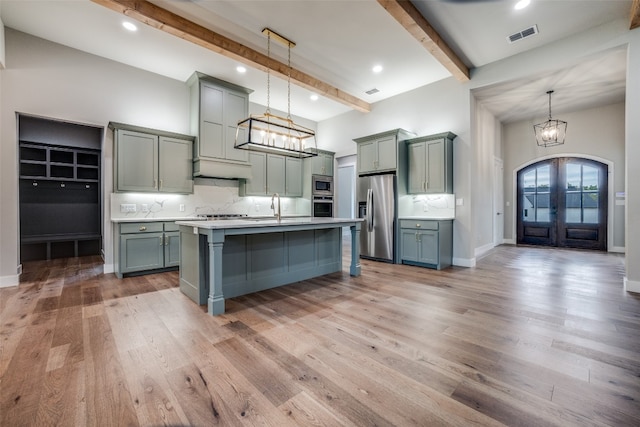 kitchen with beamed ceiling, wood-type flooring, stainless steel appliances, and decorative light fixtures