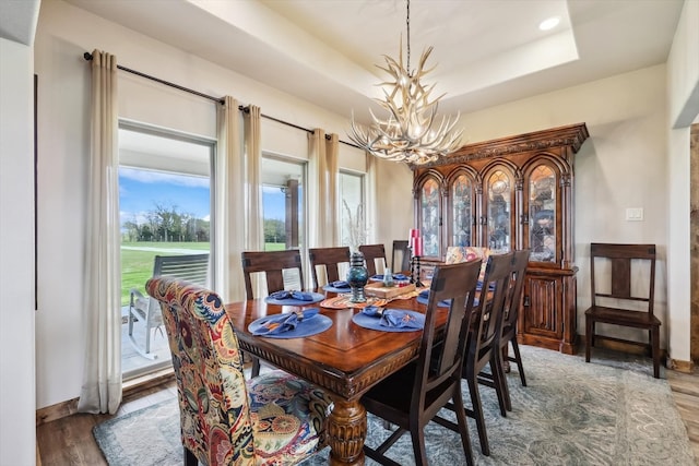 dining space featuring an inviting chandelier, a raised ceiling, and dark hardwood / wood-style flooring