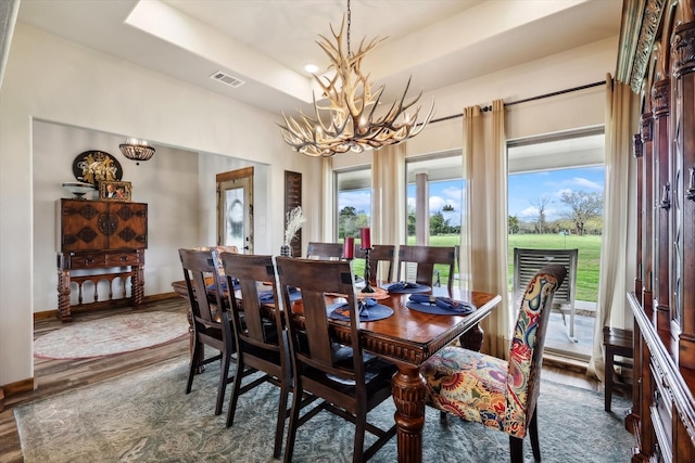 dining area featuring a notable chandelier, a raised ceiling, and dark wood-type flooring