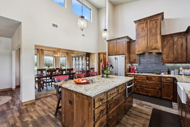 kitchen featuring a notable chandelier, a towering ceiling, appliances with stainless steel finishes, hanging light fixtures, and dark hardwood / wood-style flooring