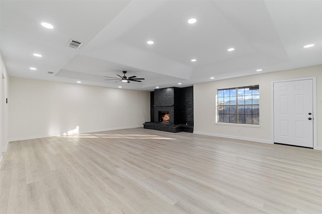 unfurnished living room with a fireplace, ceiling fan, light hardwood / wood-style flooring, and a tray ceiling