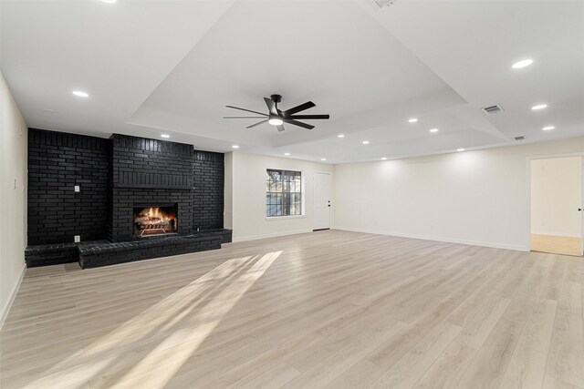 unfurnished living room featuring a fireplace, a tray ceiling, light hardwood / wood-style flooring, and ceiling fan