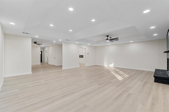 unfurnished living room featuring ceiling fan, light hardwood / wood-style floors, a raised ceiling, and a brick fireplace