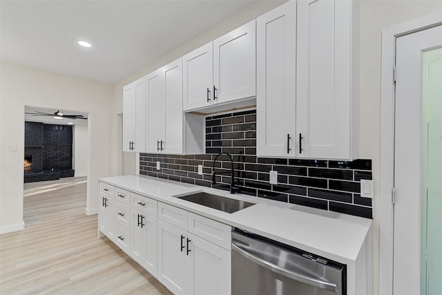 kitchen with sink, white cabinets, stainless steel dishwasher, and a brick fireplace