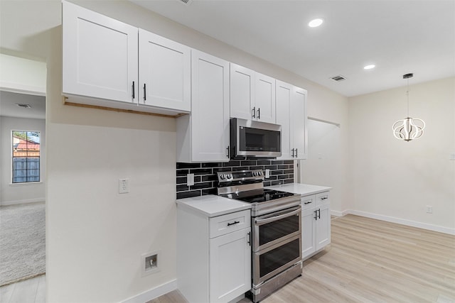 kitchen with light wood-type flooring, tasteful backsplash, stainless steel appliances, pendant lighting, and white cabinetry