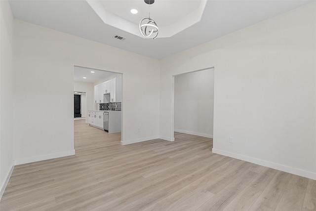 unfurnished room with light hardwood / wood-style floors, a raised ceiling, and a chandelier