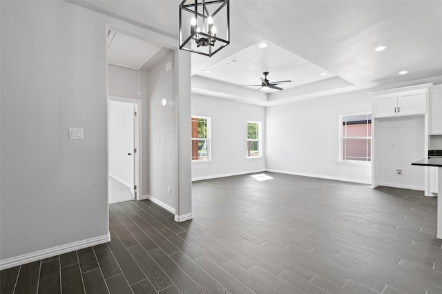 unfurnished living room featuring a raised ceiling, ceiling fan with notable chandelier, and dark hardwood / wood-style flooring