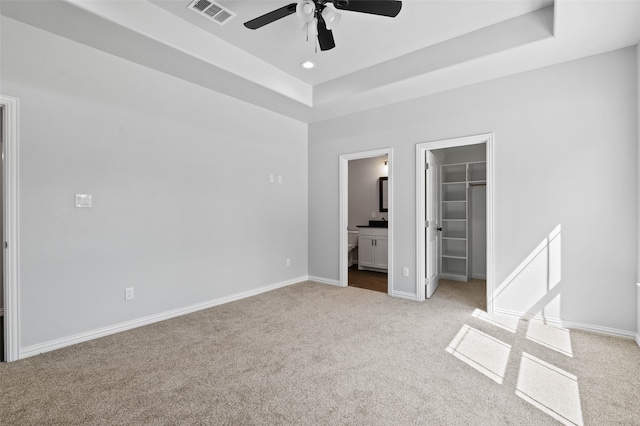 unfurnished bedroom with ensuite bath, a spacious closet, ceiling fan, light colored carpet, and a closet