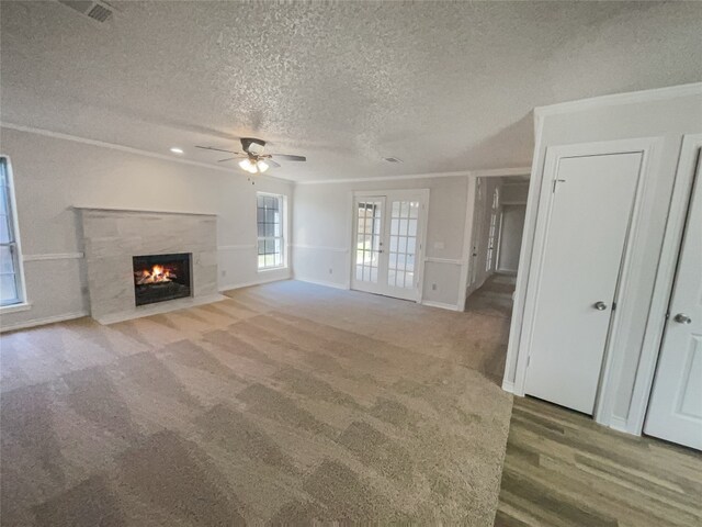 unfurnished living room with french doors, ceiling fan, a fireplace, a textured ceiling, and light wood-type flooring