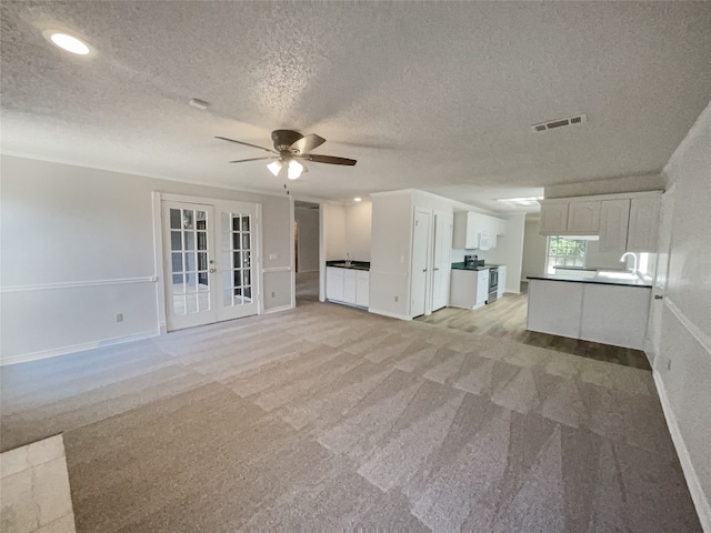 unfurnished living room with french doors, a textured ceiling, ceiling fan, and light colored carpet