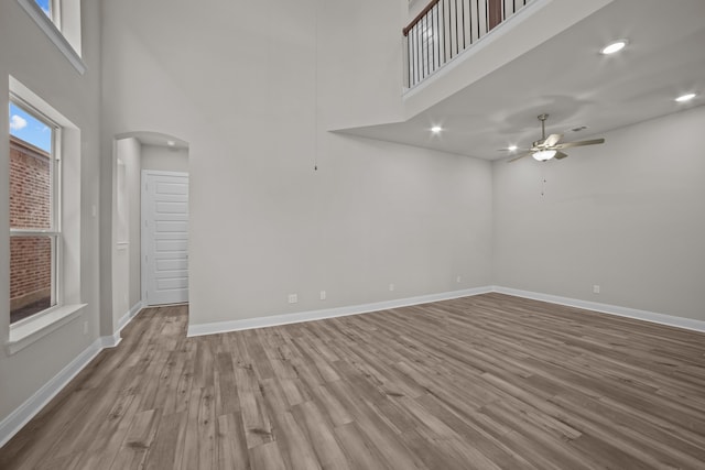 spare room featuring ceiling fan, light hardwood / wood-style flooring, a towering ceiling, and a healthy amount of sunlight