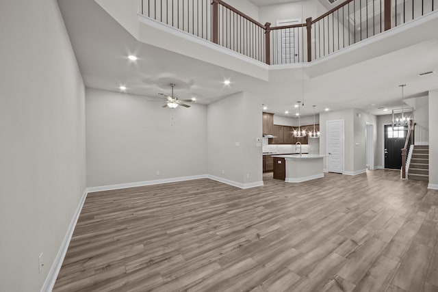 unfurnished living room with sink, ceiling fan with notable chandelier, wood-type flooring, and a high ceiling