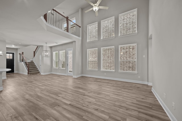 unfurnished living room featuring ceiling fan with notable chandelier, light hardwood / wood-style floors, and a high ceiling