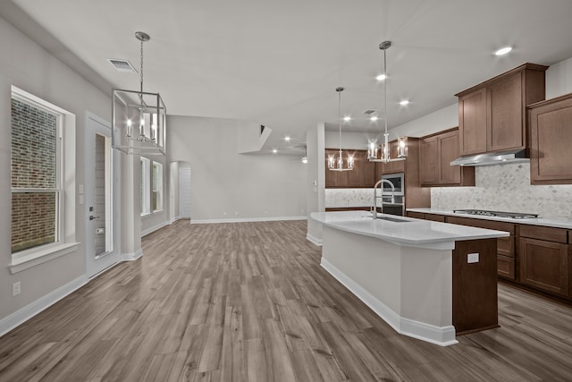 kitchen featuring decorative backsplash, stainless steel gas cooktop, a kitchen island with sink, hardwood / wood-style floors, and hanging light fixtures