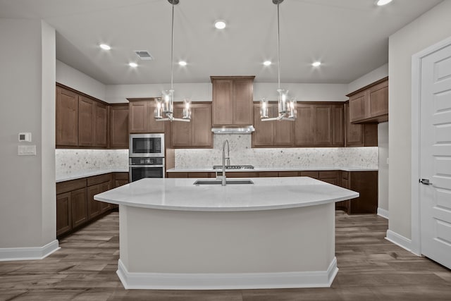 kitchen with sink, pendant lighting, a center island with sink, appliances with stainless steel finishes, and hardwood / wood-style flooring