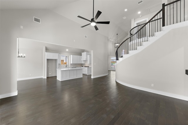 unfurnished living room featuring ceiling fan with notable chandelier, dark wood-type flooring, and high vaulted ceiling