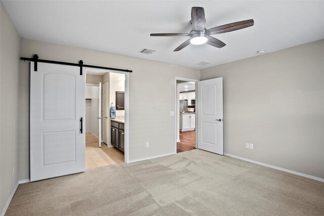 unfurnished bedroom with ceiling fan, a barn door, light carpet, and ensuite bath