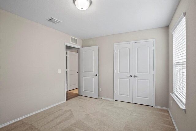 unfurnished bedroom with multiple windows, light colored carpet, and a closet