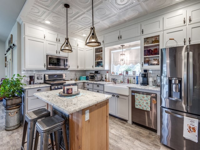 kitchen with a kitchen island, tasteful backsplash, white cabinetry, decorative light fixtures, and stainless steel appliances