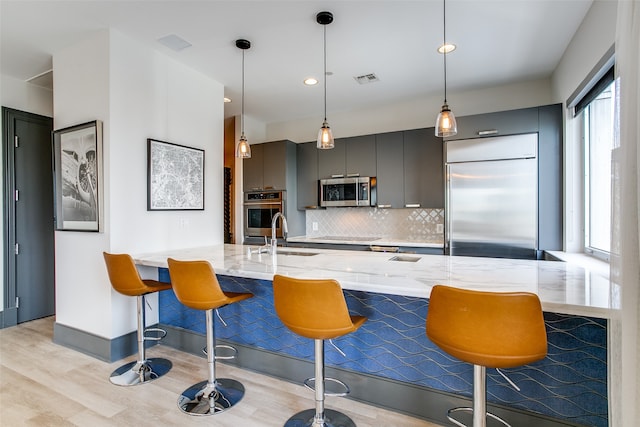 kitchen featuring appliances with stainless steel finishes, light stone counters, a kitchen bar, and sink