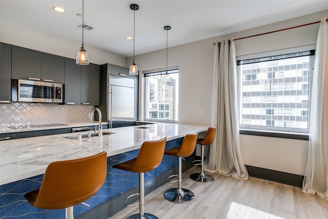 kitchen featuring stainless steel appliances, tasteful backsplash, a sink, decorative light fixtures, and light wood-type flooring