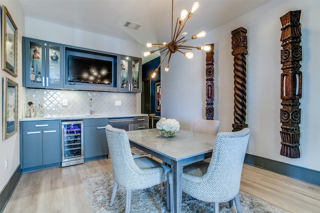 dining area with a notable chandelier, wet bar, wine cooler, and light hardwood / wood-style flooring