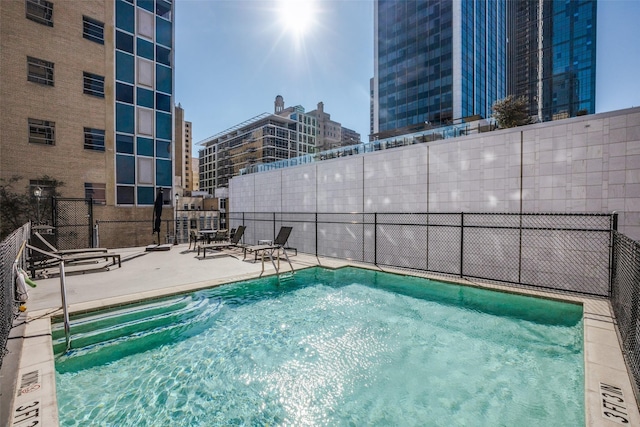 view of pool with a patio, a view of city, and fence