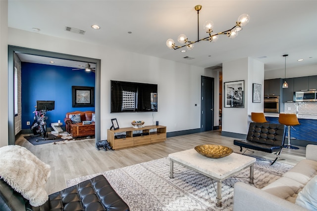 living room with ceiling fan with notable chandelier and light hardwood / wood-style flooring