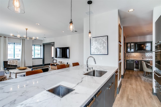 kitchen featuring pendant lighting, beverage cooler, light stone counters, and sink