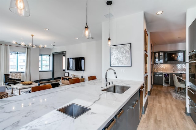 kitchen featuring open floor plan, tasteful backsplash, wine cooler, a sink, and light wood-style flooring