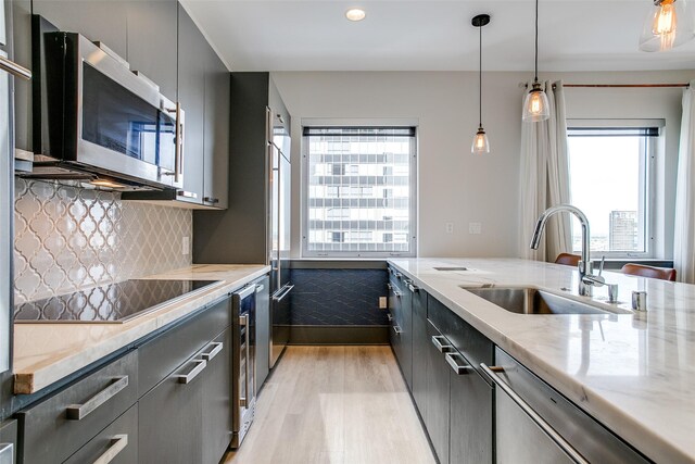 kitchen with a sink, light stone countertops, gray cabinetry, light wood-style flooring, and stainless steel appliances