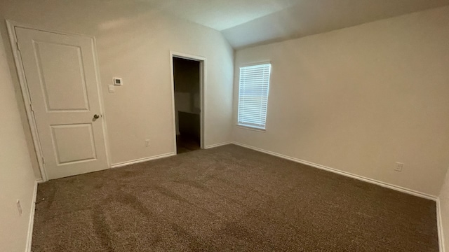 unfurnished bedroom with lofted ceiling, dark carpet, a closet, and a spacious closet