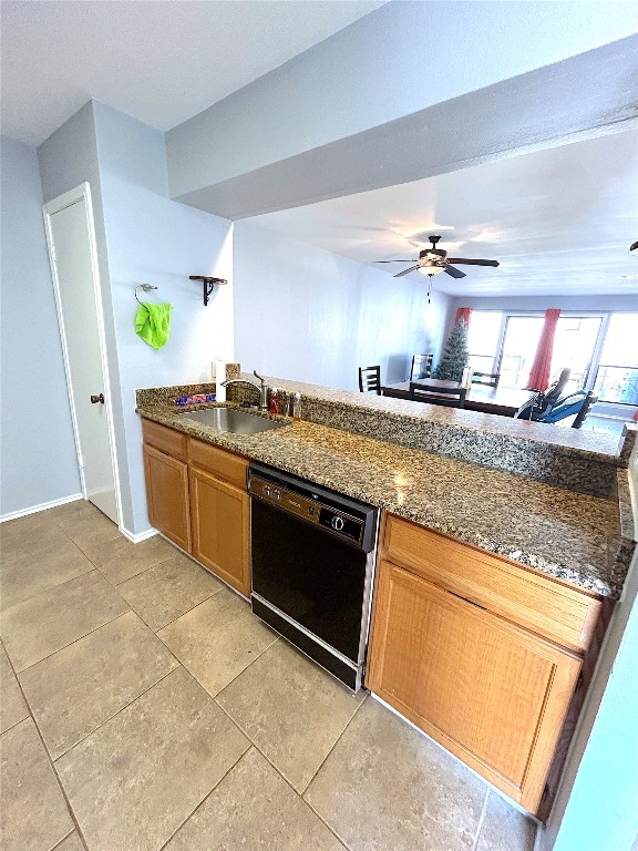 kitchen with dark stone countertops, black dishwasher, sink, ceiling fan, and light tile floors