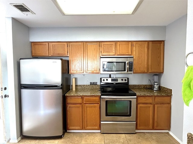 kitchen featuring dark stone countertops, appliances with stainless steel finishes, and light tile flooring