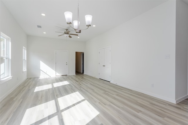 empty room with ceiling fan with notable chandelier and light wood-type flooring