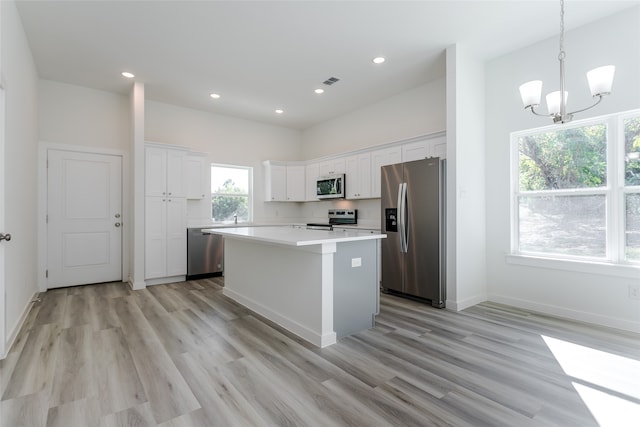 kitchen with a center island, appliances with stainless steel finishes, pendant lighting, light hardwood / wood-style floors, and white cabinets