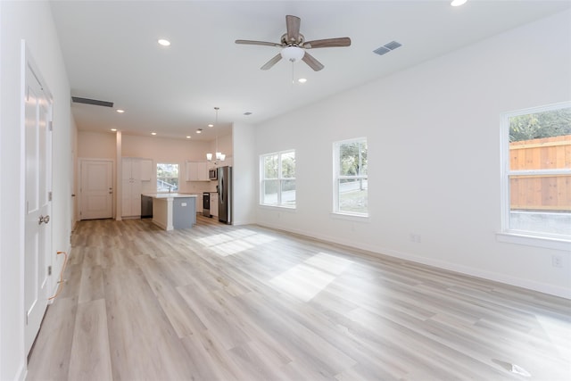 unfurnished living room with ceiling fan with notable chandelier and light hardwood / wood-style floors