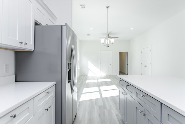 kitchen with white cabinetry, hanging light fixtures, light hardwood / wood-style flooring, stainless steel fridge, and ceiling fan