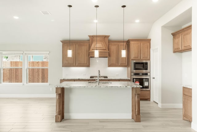 kitchen with hanging light fixtures, light stone counters, a center island with sink, custom range hood, and appliances with stainless steel finishes