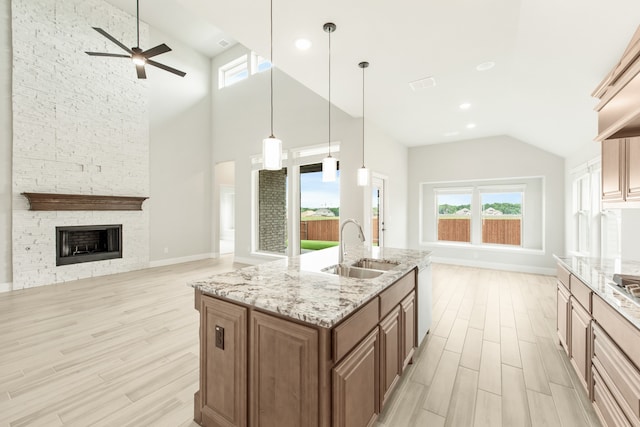 kitchen featuring ceiling fan, sink, a stone fireplace, decorative light fixtures, and light wood-type flooring