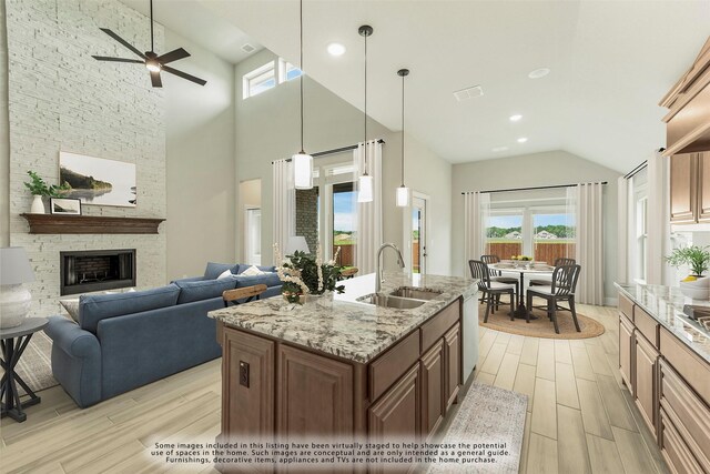 kitchen featuring a stone fireplace, light wood-type flooring, sink, and an island with sink