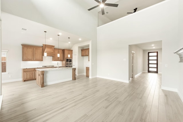 kitchen with ceiling fan, light hardwood / wood-style flooring, a towering ceiling, an island with sink, and custom exhaust hood