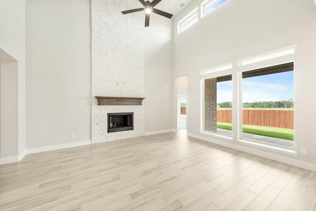 unfurnished living room featuring ceiling fan, light wood-type flooring, a fireplace, and a high ceiling