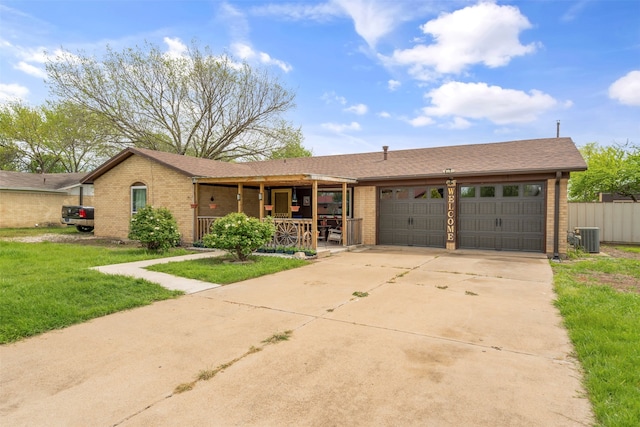 ranch-style house featuring a front yard, covered porch, central AC unit, and a garage