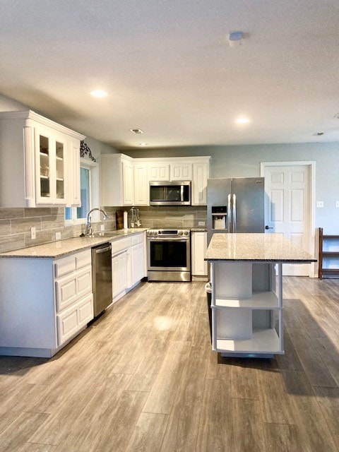 kitchen featuring appliances with stainless steel finishes, light hardwood / wood-style floors, white cabinets, light stone countertops, and sink